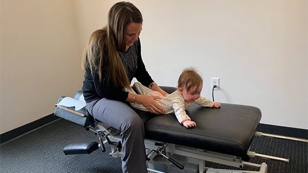 Chiropractor Edina MN Mackenzie Arellanes Adjusting Infant Welcome to Our Clinic Mackenzie Arellanes is seen adjusting a baby and both are smiling and laughing